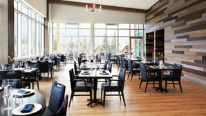 A spacious dining area with multiple tables and chairs, large windows, and a modern ceiling light fixture. - ★Mountain Haven★Pool&HotTub☆King Bed☆AC☆BBQ/Patio! (Canmore)