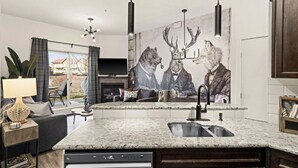 Cocina moderna con encimera de granito, lavavajillas integrado y un amplio ventanal con cortinas.