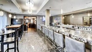 Un moderno lobby de hotel con una zona de bar, arreglos de asientos y una entrada visible a otra sección.