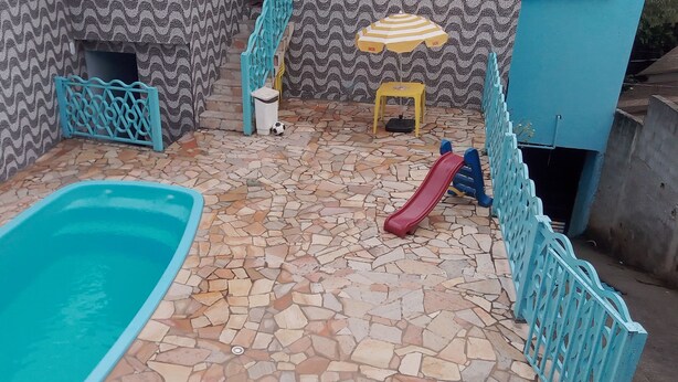 A swimming pool with a slide, a small table with an umbrella, and a patterned wall. - Casa com Piscina em Mairiporã , (Mairiporã)