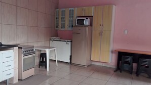 A compact kitchen with a stove, microwave, and refrigerator, a small table, and a stool. - Casa com Piscina em Mairiporã , (Mairiporã)