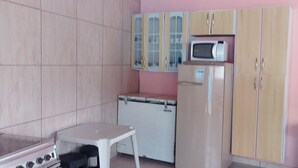 A kitchen with a gas stove, a microwave, and a refrigerator. There is a small table and cabinets with a pink wall. - Casa com Piscina em Mairiporã , (Mairiporã)