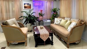 A living room with a sofa, two armchairs, a coffee table, and a potted plant. - Olympia Inn  (Colorado Springs)