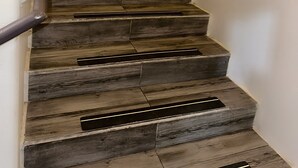 A wooden staircase with a metal handrail and a vent at the bottom. - Olympia Inn  (Colorado Springs)