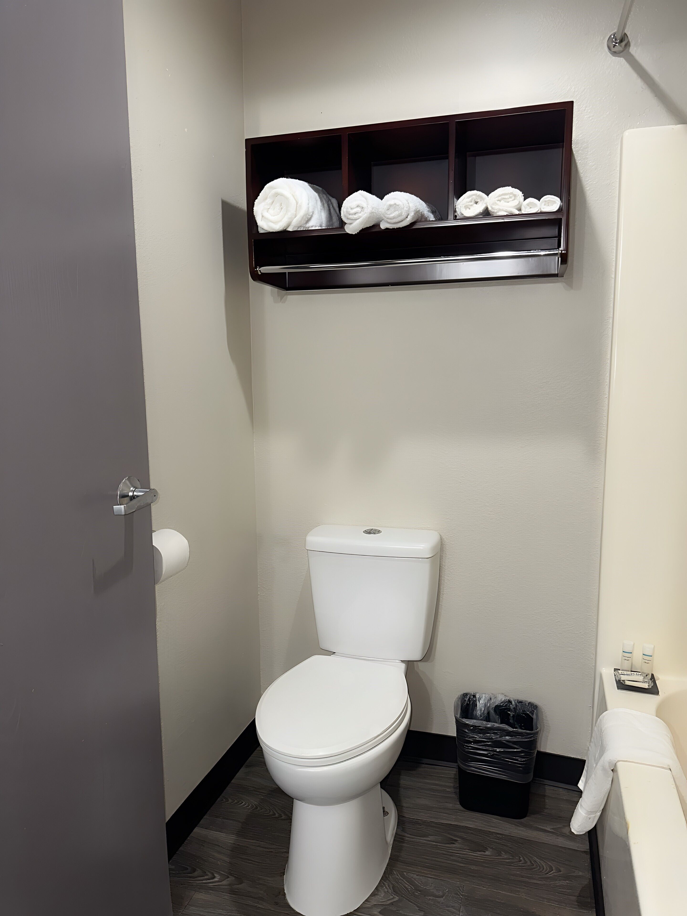 Un bagno con un WC bianco, uno scaffale con asciugamani arrotolati, un cestino nero e un porta asciugamani bianco.