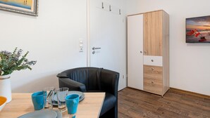 Une chambre moderne avec une table à manger en bois, dressée pour deux personnes, une chaise en cuir noir, une armoire blanche avec un panneau en bois et un tableau encadré accroché au mur.
