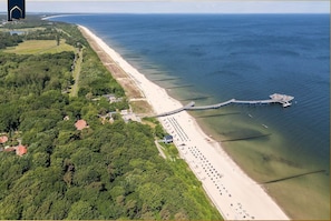 Eine Luftaufnahme einer Küstenlandschaft mit Strand, einer Mole und umgebender Bepflanzung.