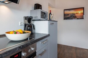 A modern kitchen with a digital clock, a bowl of fruit, a coffee maker, and a wine bottle. - Ferienwohnung 02 - Kimpi (Koserow)