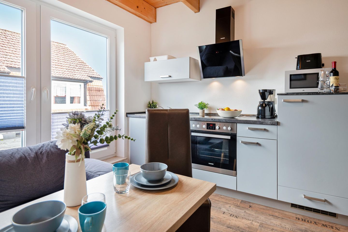 Een moderne keuken met een ingebouwde oven, magnetron en een eethoek met tafel en stoelen.
