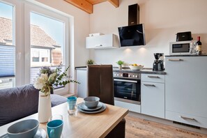 A modern kitchen with a built-in oven, microwave, and a dining area with a table and chairs. - Ferienwohnung 02 - Kimpi (Koserow)