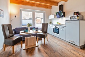 A modern kitchen with a built-in oven, microwave, and a small refrigerator. There is a dining area with a table and chairs, and a sofa. - Ferienwohnung 02 - Kimpi (Koserow)