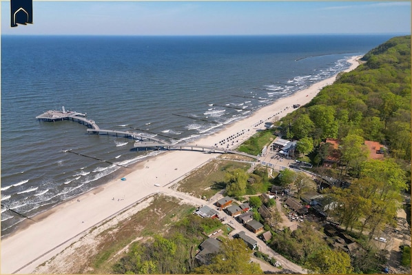 An aerial view of a coastal area with a beach, a pier, and residential buildings.