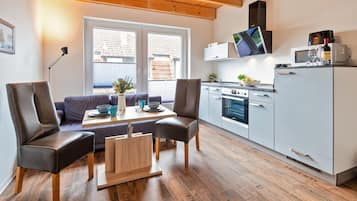 Een moderne keuken met een inbouwoven, magnetron en een kleine koelkast. Er is een eethoek met een tafel en stoelen, en een bank.