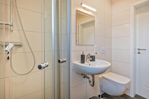 Un baño moderno con cabina de ducha de vidrio, un lavabo blanco y un inodoro.