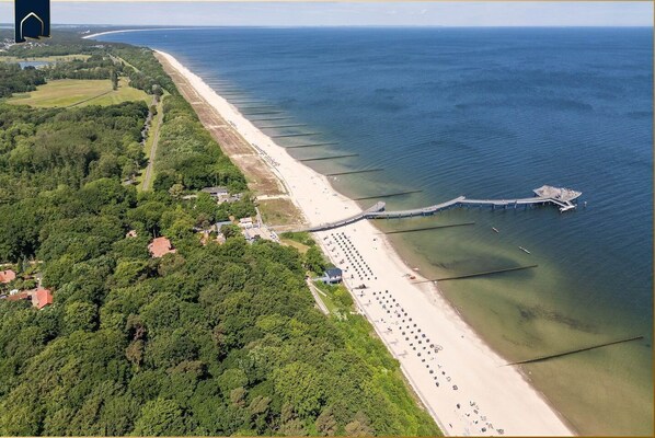Vista aérea de una zona costera con playa, muelle y vegetación circundante.