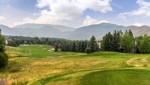 A golf course with rolling hills, trees, and distant mountains under a clear sky. - Modern Golf View Condo + Resort Amenities (Sun Valley)