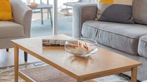 A modern living room with a wooden coffee table, a grey sofa, and a glass bowl with decorative items. - Beachside 2BR condo w/ lanais & free parking (Honolulu)