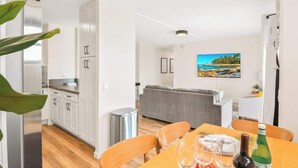 A modern kitchen with white cabinets, a dining area with a table set for two, and a grey sofa in the living area. - Beachside 2BR condo w/ lanais & free parking (Honolulu)