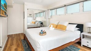 A hotel room with a bed, a nightstand, a ceiling fan, a window, and a door. - Beachside 2BR condo w/ lanais & free parking (Honolulu)