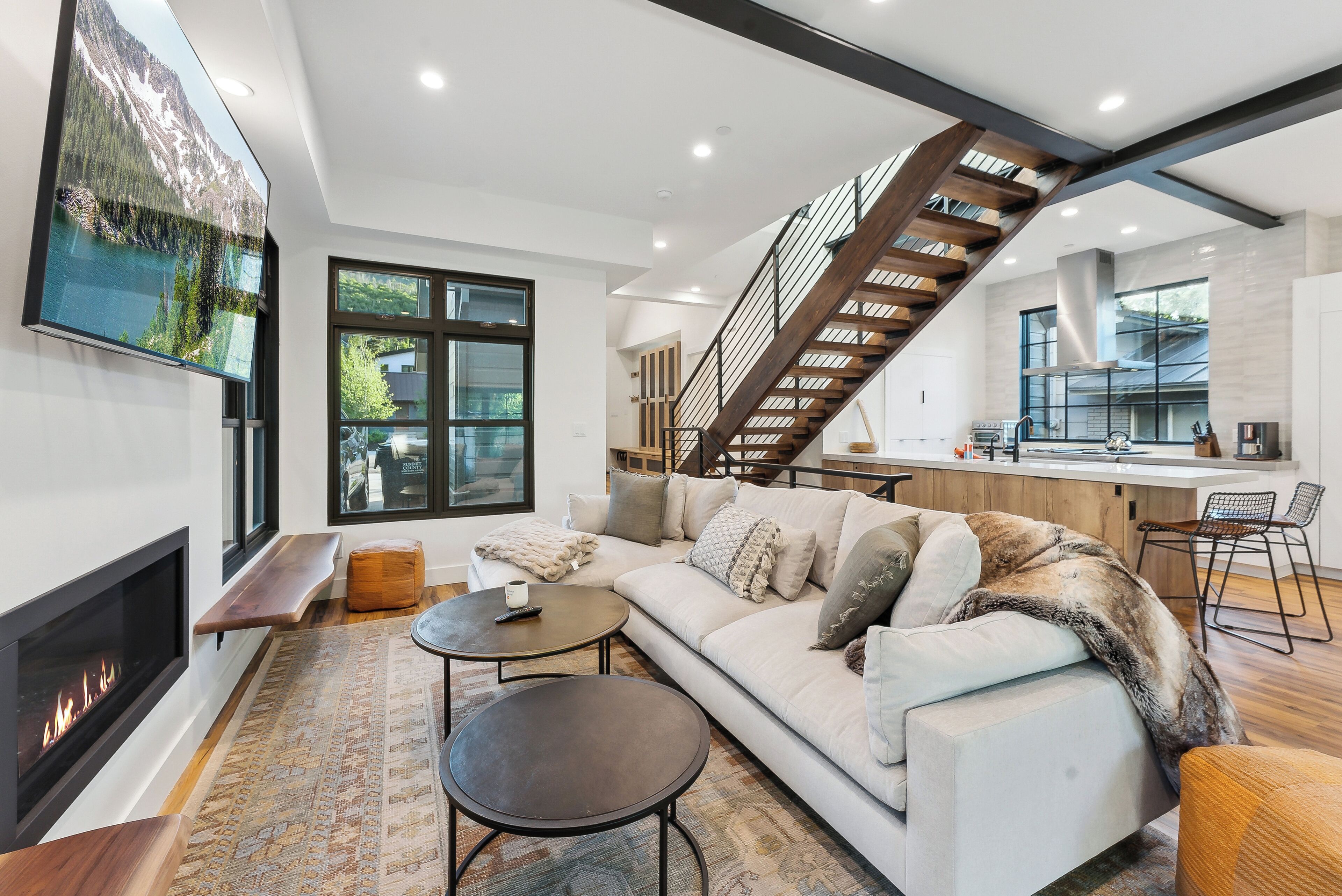 A modern living room with a fireplace, a sofa, a coffee table, and a staircase leading to the kitchen.