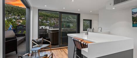 Een moderne keuken met een groot schiereiland, schuiframen naar een balkon en uitzicht op een heuvelstad.