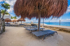 A beachside area with lounge chairs, thatched umbrellas, and a view of the ocean. - The Queen of Cozumel`s  Coastal Crown OCEAN FRONT (Cozumel)