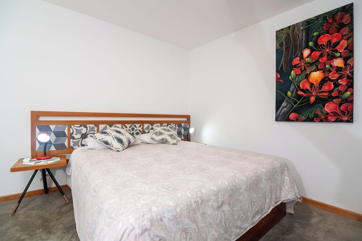 A bedroom with a bed, a nightstand with a lamp, and a wall-mounted painting.