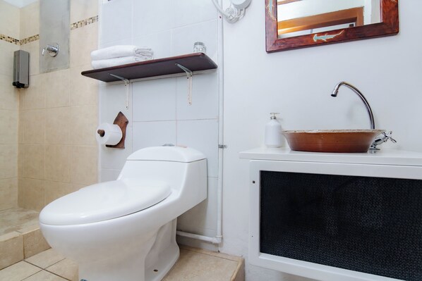 A bathroom with a toilet, a sink with a basin, a shelf with towels, and a mirror. - La k-leta Boutique guesthouse (Puerto Ayora)