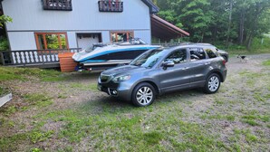 Un SUV gris estacionado frente a una casa con un barco sobre un remolque.