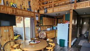 Interior de una cabaña de madera con comedor, cocina y un pequeño espacio de sala.