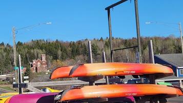 Een rij kleurrijke kajaks geparkeerd buiten, met een heldere lucht en een gebouw op de achtergrond.