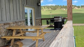 Una terraza de madera con una mesa de picnic y una parrilla, con vista a un campo verde.