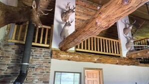 Un interior rústico con vigas de madera, paredes de piedra y ciervos colgados.