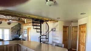 Una cocina con una isla central, taburetes de bar, chimenea y una escalera de caracol.