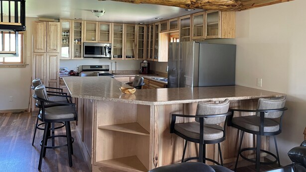 Una cocina moderna con armarios de madera, una isla grande con taburetes de bar, electrodomésticos de acero inoxidable y un techo rústico.