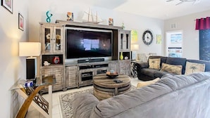 A modern living room with a large flat-screen TV, wooden cabinets, a grey sofa, and a ceiling fan. - Sunset Sanctuary (Davenport)