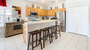 A modern kitchen with wooden cabinets, stainless steel appliances, and a central island with bar stools. - Sunset Sanctuary (Davenport)