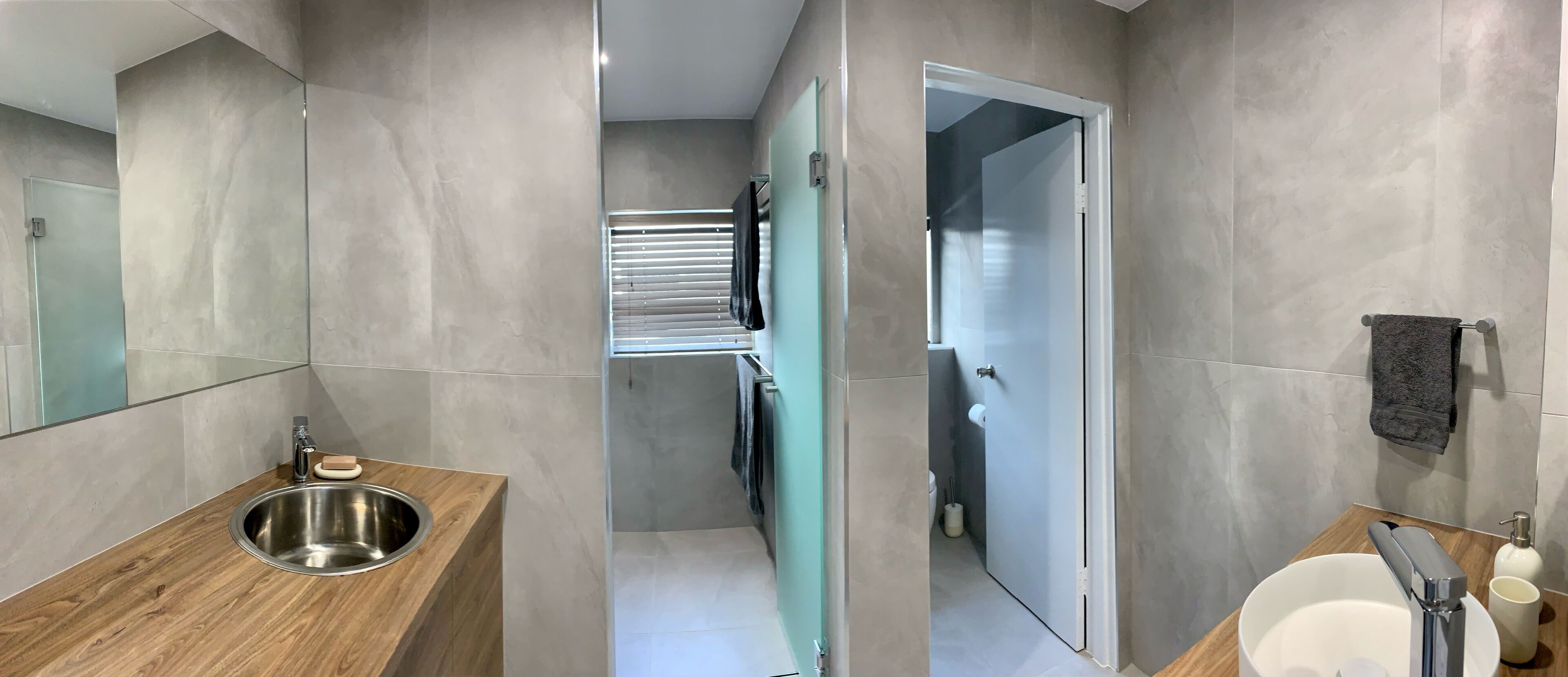 Un baño moderno con un mueble de tocador de madera, un lavamanos de acero inoxidable, un cerramiento de ducha de vidrio y un inodoro blanco.