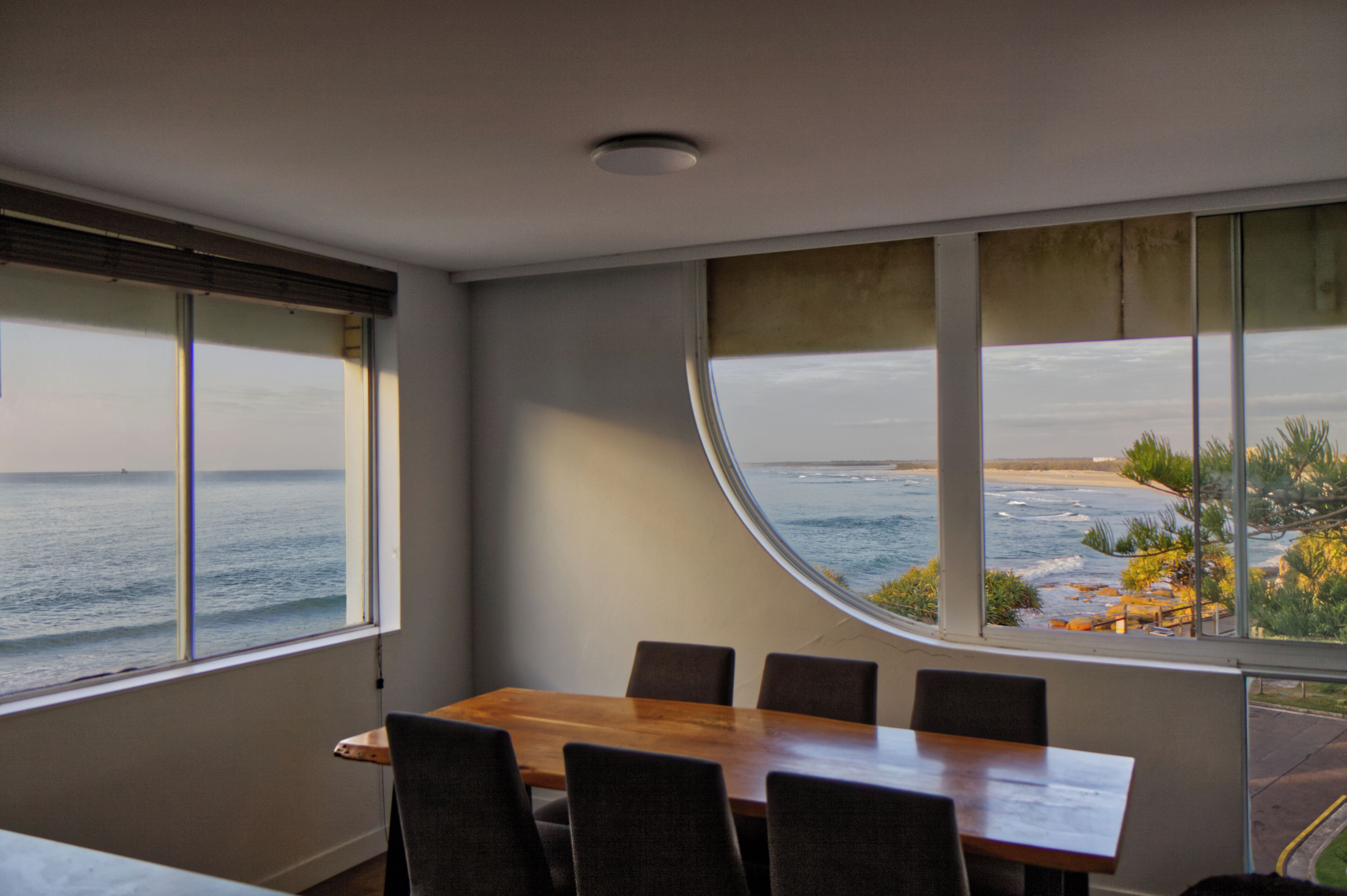 A dining area with a table and chairs, large windows with ocean views, and a ceiling light.
