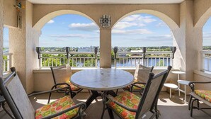 Un balcon avec une table ronde et des chaises, des fenêtres en arc de cercle et une vue sur une rivière et la verdure.