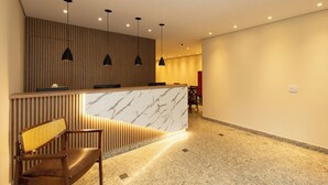 A reception area with a marble counter, wooden slatted wall, and a seating area with a bench and chair. - Villa Jequitibá Hotel (São Paulo)
