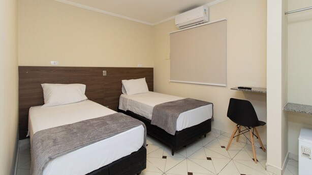 A hotel room with two single beds, a small desk, a chair, and a toilet. - Villa Jequitibá Hotel (São Paulo)