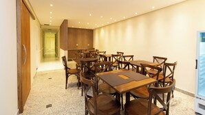 Un espace repas avec des tables et des chaises en bois, un coin cuisine avec des placards en bois et un réfrigérateur.