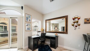 Un bureau à domicile équipé d’un bureau, d’une chaise et d’un grand miroir. Il y a une fenêtre avec des stores, un tapis et des œuvres d’art accrochées aux murs.