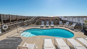 Un espace piscine avec des chaises longues blanches, une terrasse en bois et un poste de surveillance pour les sauveteurs.