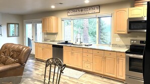 Una cocina moderna con armarios de madera, un horno de acero inoxidable y un amplio ventanal con vistas a árboles.
