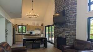 Een ruime woonkamer met een stenen openhaard, leren banken en een moderne keuken op de achtergrond.