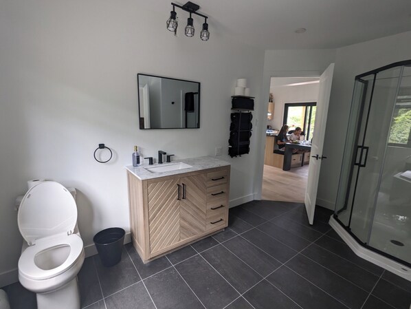 Een moderne badkamer met een wit toilet, een houten wastafelmeubel met een wastafel en een douchecabine met glazen wanden.