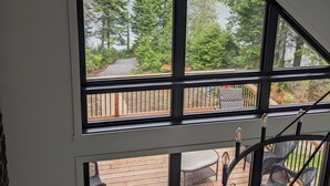 Een kamer met een groot raam dat uitkijkt op een terras met rieten meubels en uitzicht op een bebost gebied.