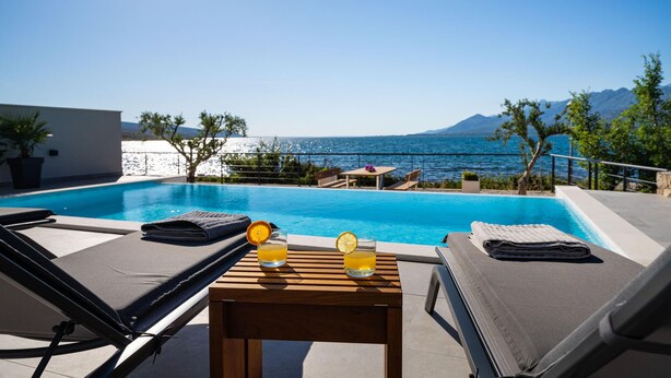 A rooftop pool with lounge chairs, a table with drinks, and a view of the sea and mountains. - Lovely apartment in Rovanjska (Rovanjska)
